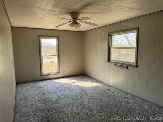 empty room with carpet floors, ceiling fan, visible vents, and a wealth of natural light