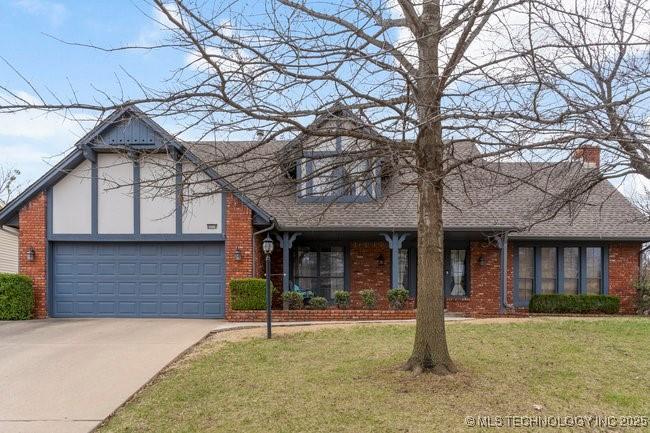 6218 E 77th Pl, Tulsa, OK 74136 - english style home with a front yard, driveway, roof with shingles, a garage, and brick siding