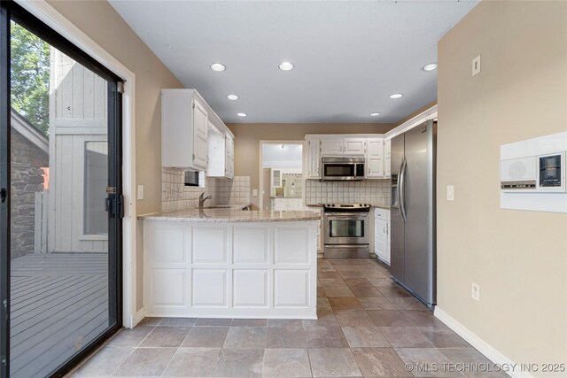 6505 S Oswego Ave, Tulsa, OK 74136 - kitchen with white cabinets, a peninsula, stainless steel appliances, and decorative backsplash