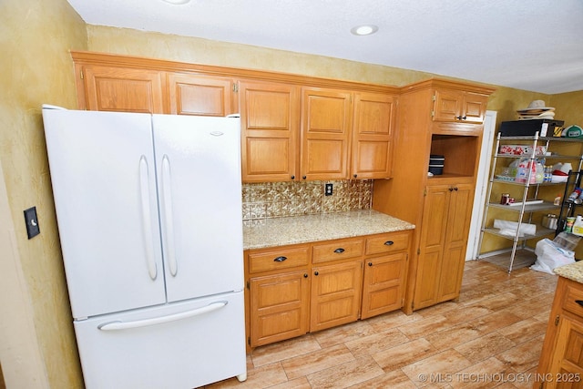 1430 Williams St, Fort Gibson, OK 74434 - kitchen with brown cabinetry, decorative backsplash, freestanding refrigerator, and light stone countertops