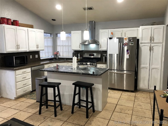 kitchen with a sink, stainless steel appliances, white cabinets, and wall chimney range hood