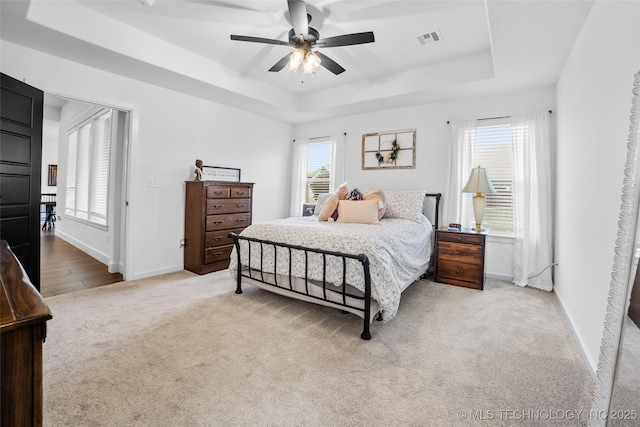 carpeted bedroom featuring visible vents, ceiling fan, a tray ceiling, and baseboards