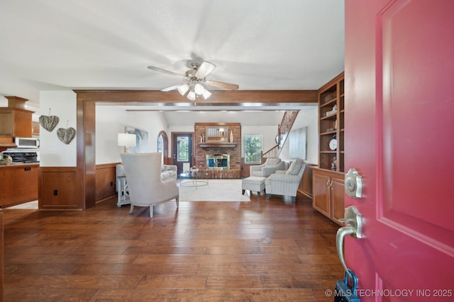 11712 E 121st St, Collinsville, OK 74021 - living room featuring dark wood finished floors, ceiling fan, wainscoting, and a brick fireplace