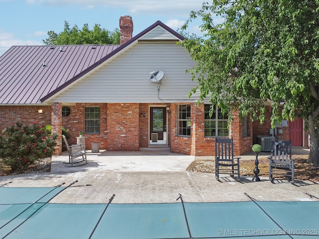 11712 E 121st St, Collinsville, OK 74021 - rear view of house with central AC unit, a patio, a chimney, and brick siding