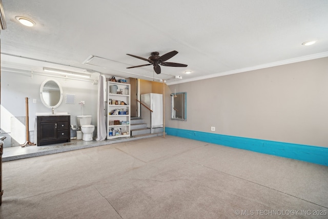 unfurnished living room featuring a ceiling fan, carpet floors, attic access, a sink, and ornamental molding