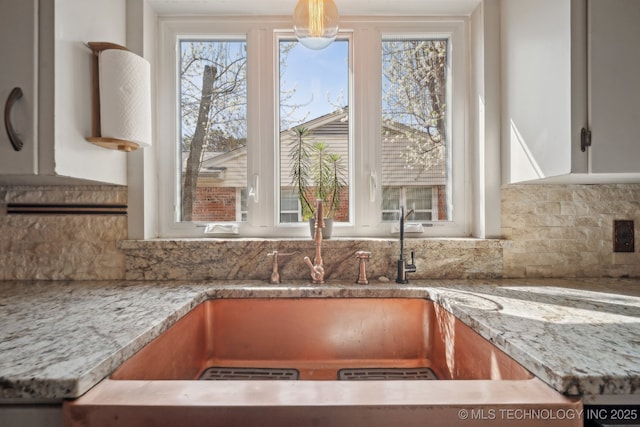 kitchen featuring light stone counters, decorative backsplash, white cabinetry, and a sink