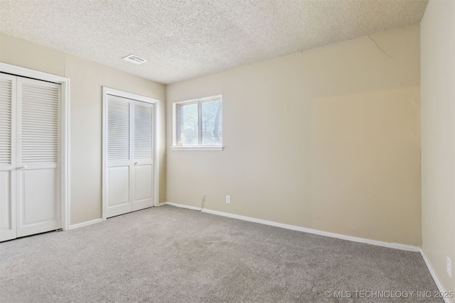 unfurnished bedroom featuring carpet, baseboards, visible vents, a textured ceiling, and two closets
