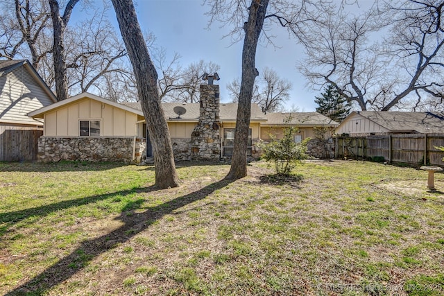 back of property featuring stone siding, a lawn, board and batten siding, and fence