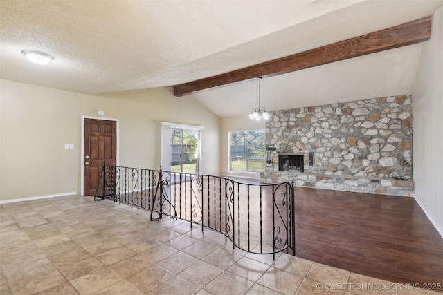 tiled empty room featuring vaulted ceiling with beams, baseboards, a fireplace, a notable chandelier, and a textured ceiling
