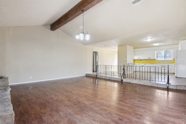 unfurnished living room with visible vents, vaulted ceiling with beams, baseboards, wood finished floors, and a textured ceiling