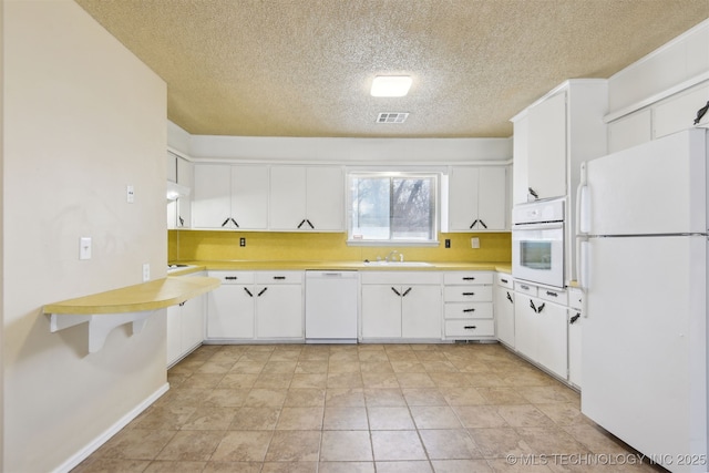 kitchen with a sink, visible vents, white appliances, and light countertops