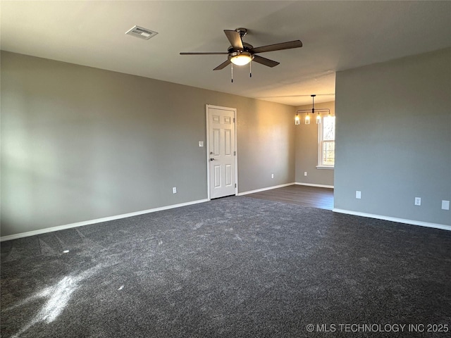empty room featuring ceiling fan with notable chandelier, visible vents, dark colored carpet, and baseboards