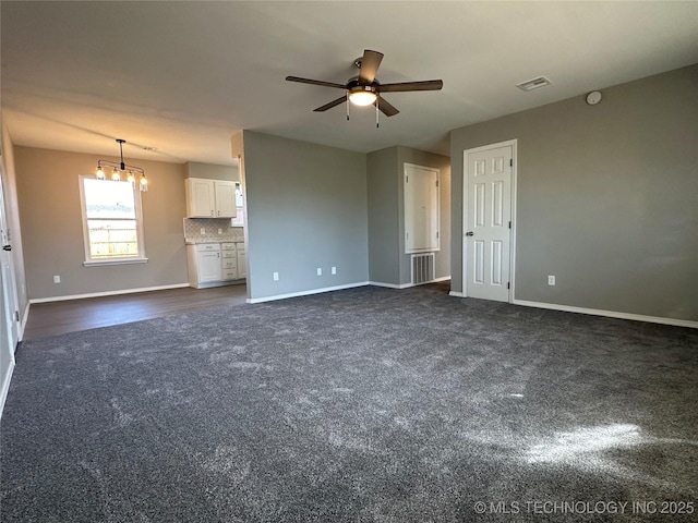 unfurnished living room featuring visible vents, ceiling fan with notable chandelier, baseboards, and dark colored carpet