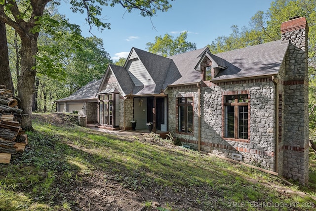 view of front of home with a chimney, an attached garage, roof with shingles, and stone siding