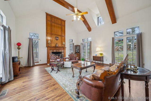 living room featuring light wood-type flooring, visible vents, a brick fireplace, ceiling fan, and high vaulted ceiling