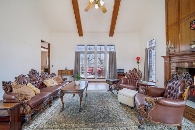 living area featuring high vaulted ceiling, a ceiling fan, wood finished floors, beamed ceiling, and a fireplace