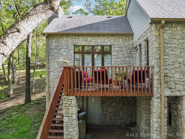 rear view of property with roof with shingles, stone siding, and stairway