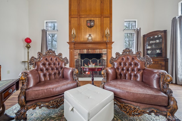 living area with wood finished floors, a brick fireplace, and a towering ceiling