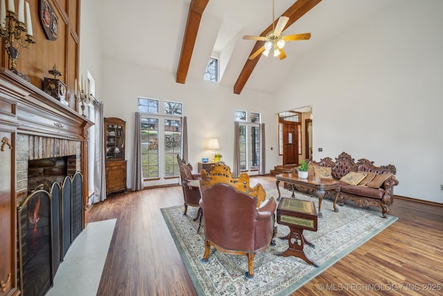 living room featuring high vaulted ceiling, a ceiling fan, wood finished floors, beamed ceiling, and a brick fireplace