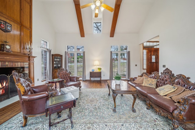 living area with wood finished floors, beam ceiling, a brick fireplace, high vaulted ceiling, and ceiling fan