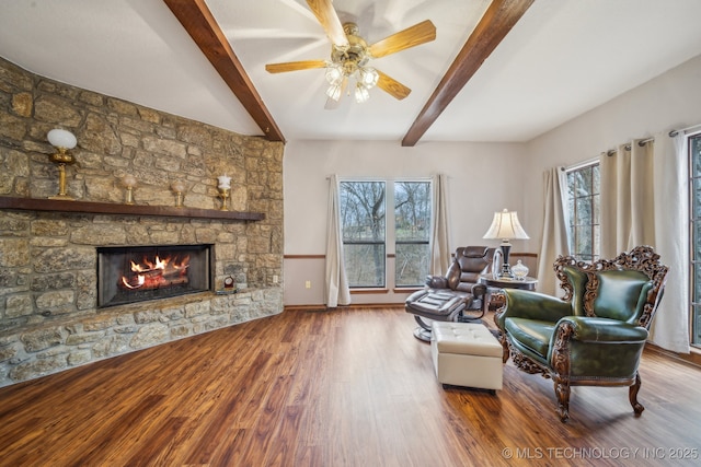 living room with beamed ceiling, wood finished floors, a ceiling fan, and a stone fireplace