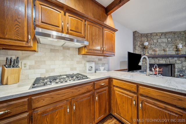 kitchen featuring light stone counters, under cabinet range hood, a sink, stainless steel gas cooktop, and decorative backsplash