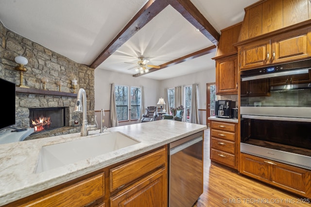 kitchen featuring light stone counters, stainless steel appliances, a sink, beamed ceiling, and open floor plan