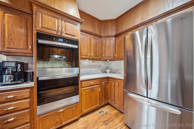 kitchen featuring decorative backsplash, light countertops, brown cabinets, and appliances with stainless steel finishes