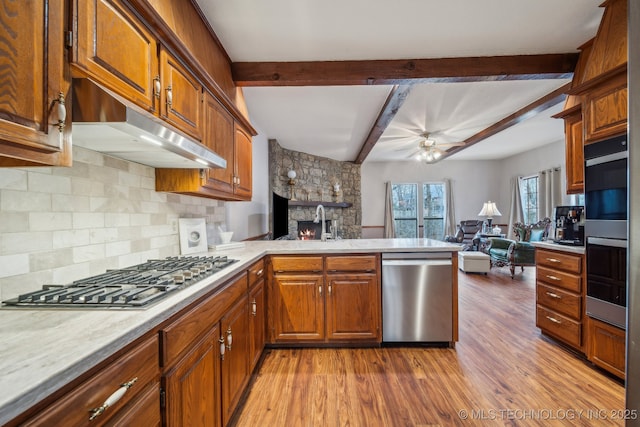 kitchen with open floor plan, appliances with stainless steel finishes, light countertops, a fireplace, and under cabinet range hood