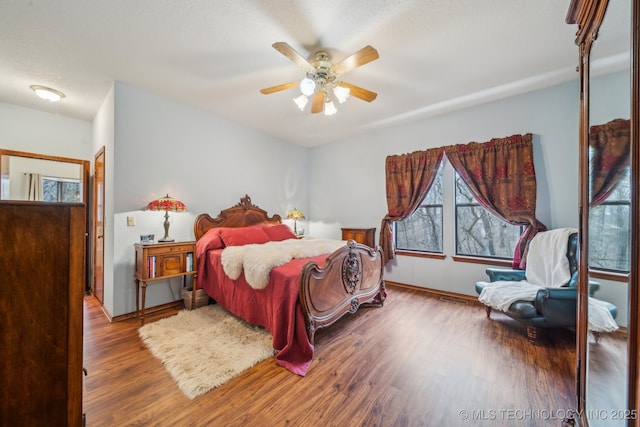 bedroom featuring baseboards, a ceiling fan, wood finished floors, and multiple windows