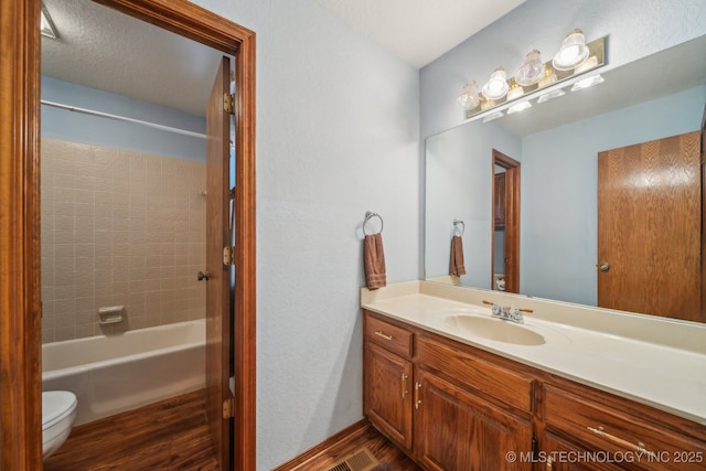 bathroom featuring toilet, vanity, wood finished floors, and shower / tub combination