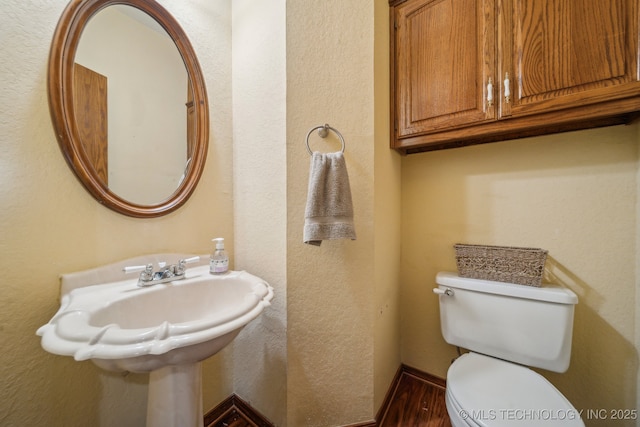 half bathroom featuring toilet, a textured wall, and wood finished floors