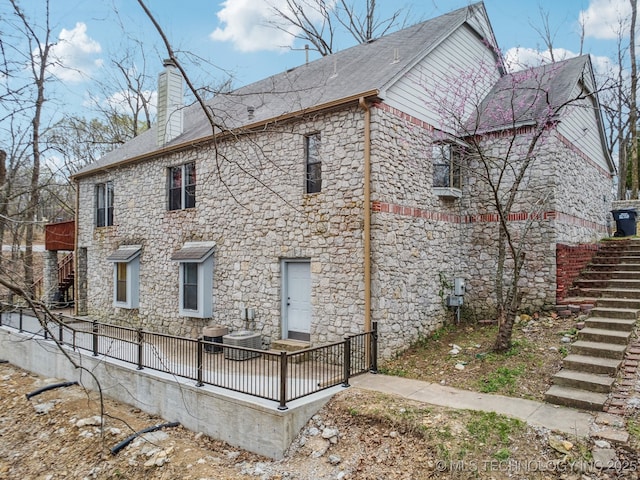 rear view of property featuring stone siding, a shingled roof, a chimney, and stairs
