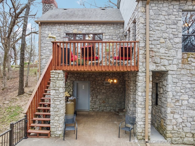 rear view of property featuring a chimney, a patio area, stone siding, and stairs