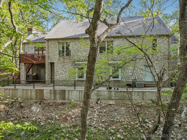 back of house with a chimney, stone siding, a shingled roof, a wooden deck, and stairs