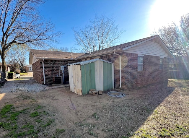 rear view of house with an outdoor structure, brick siding, a storage unit, and cooling unit