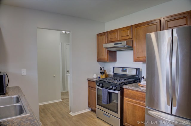 46 S 188th E Ave, Tulsa, OK 74108 - kitchen with under cabinet range hood, brown cabinets, stainless steel appliances, and light wood-style flooring