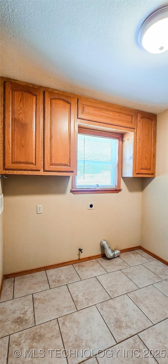 laundry area with light tile patterned flooring, cabinet space, a textured ceiling, and baseboards