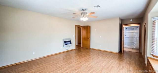 unfurnished bedroom featuring heating unit, a ceiling fan, wood finished floors, visible vents, and baseboards