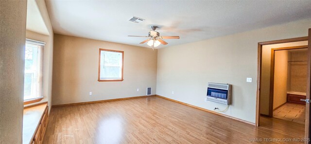 spare room featuring visible vents, heating unit, wood finished floors, baseboards, and ceiling fan