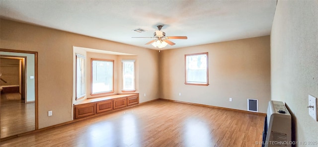 empty room featuring heating unit, light wood-type flooring, visible vents, and ceiling fan