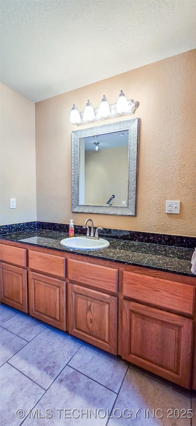bathroom with tile patterned flooring, a textured ceiling, vanity, and a textured wall