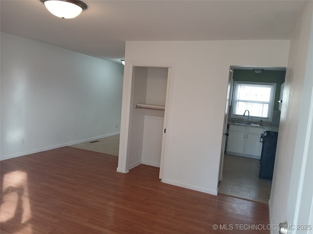 unfurnished bedroom featuring a closet, visible vents, baseboards, wood finished floors, and a sink