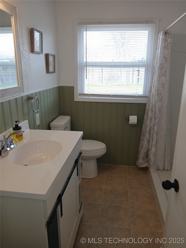 bathroom with vanity, toilet, a shower with shower curtain, a wainscoted wall, and tile patterned floors
