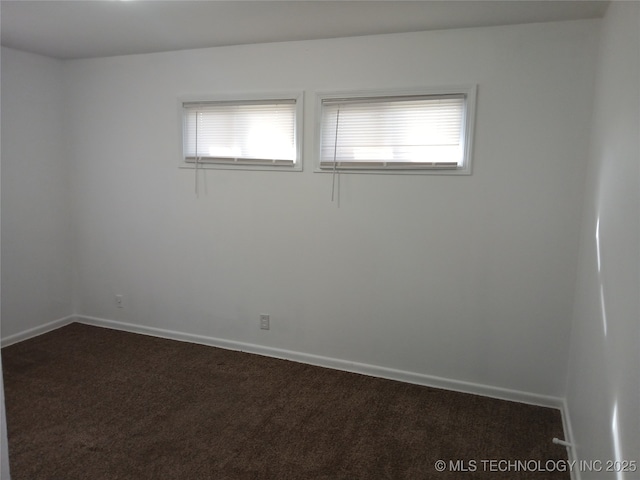spare room with a wealth of natural light, dark carpet, and baseboards
