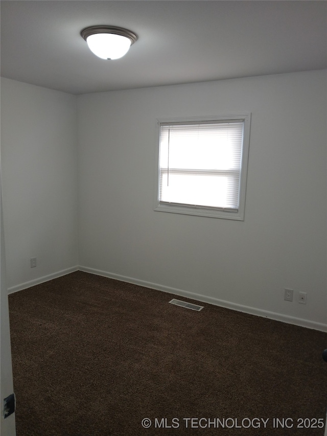 unfurnished room with baseboards, dark colored carpet, and visible vents