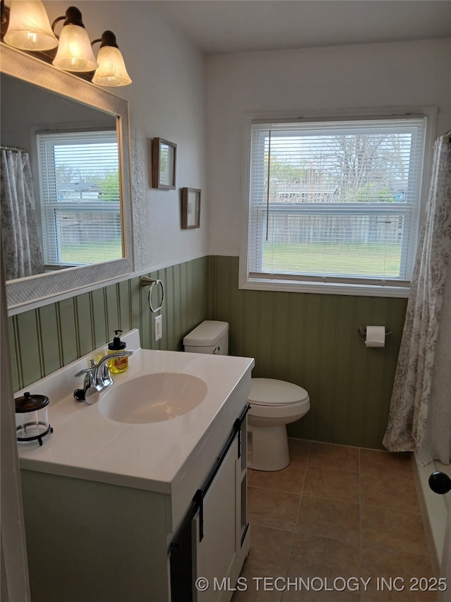 full bath featuring tile patterned floors, vanity, toilet, and wainscoting