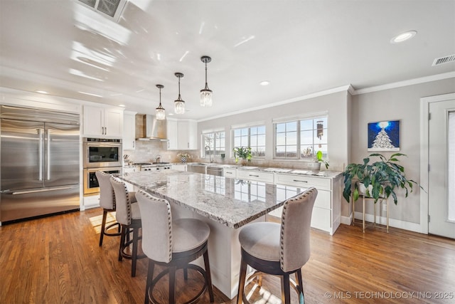 122 Osage Ridge Dr, Sand Springs, OK 74063 - kitchen with visible vents, a kitchen breakfast bar, wood finished floors, appliances with stainless steel finishes, and wall chimney range hood