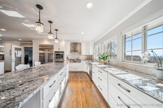 122 Osage Ridge Dr, Sand Springs, OK 74063 - kitchen with wall chimney range hood, ornamental molding, decorative backsplash, stainless steel appliances, and white cabinetry