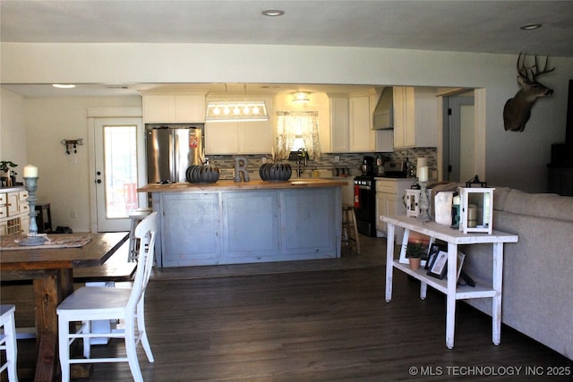 kitchen featuring dark wood-style floors, stainless steel appliances, wall chimney range hood, wood counters, and decorative backsplash